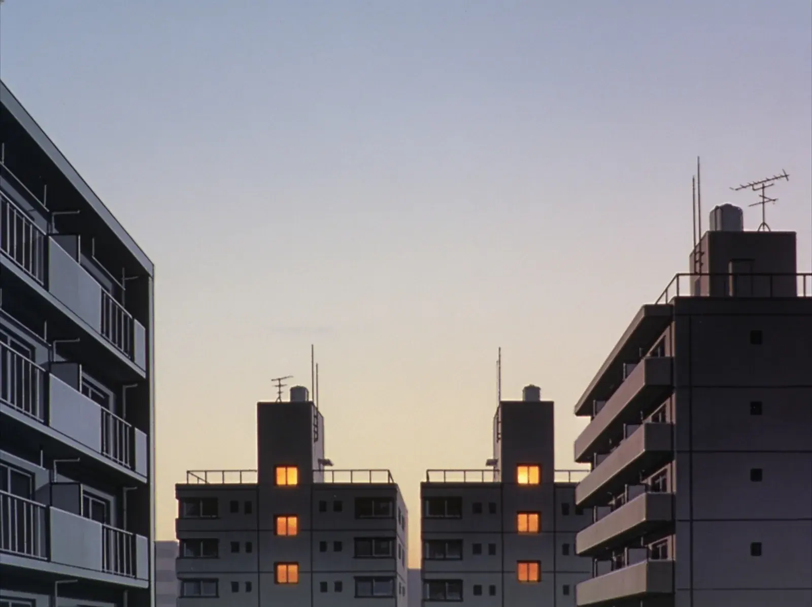 Four lit windows across separate buildings in a city at dawn, seen from a rooftop